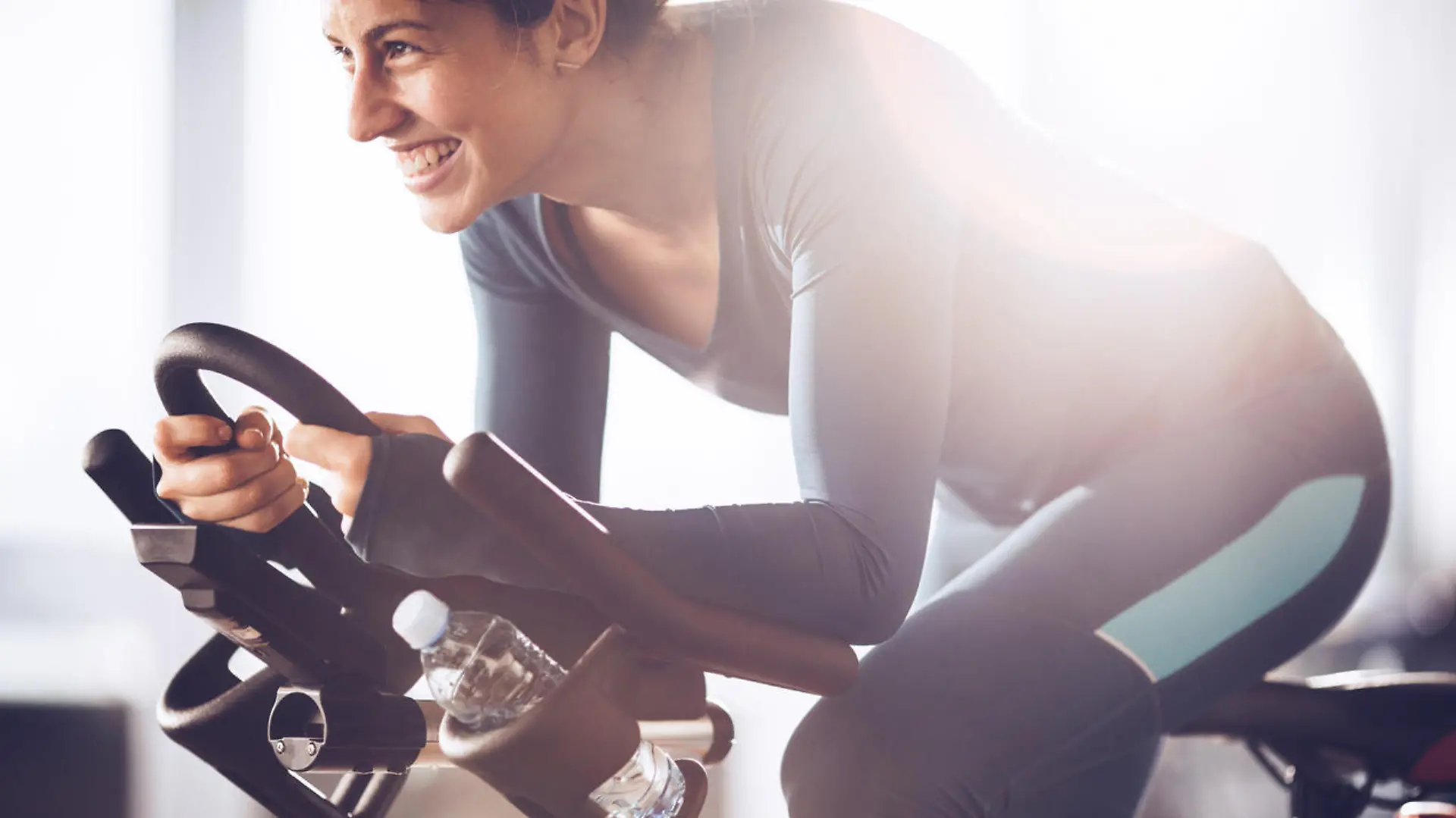 Happy athletic woman cycling on exercise bike in a gym.