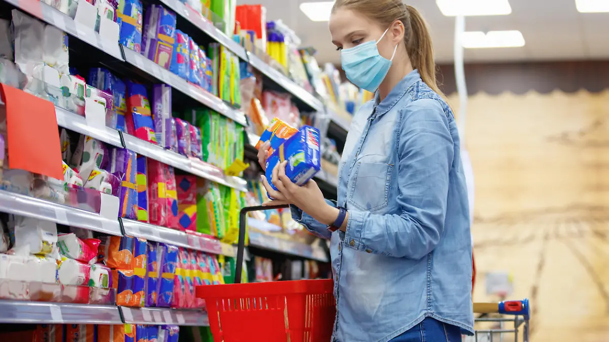 Young woman wearing protective face mask, choosing sanitary pads in supermarket aisle, COVID-19 pandemic era