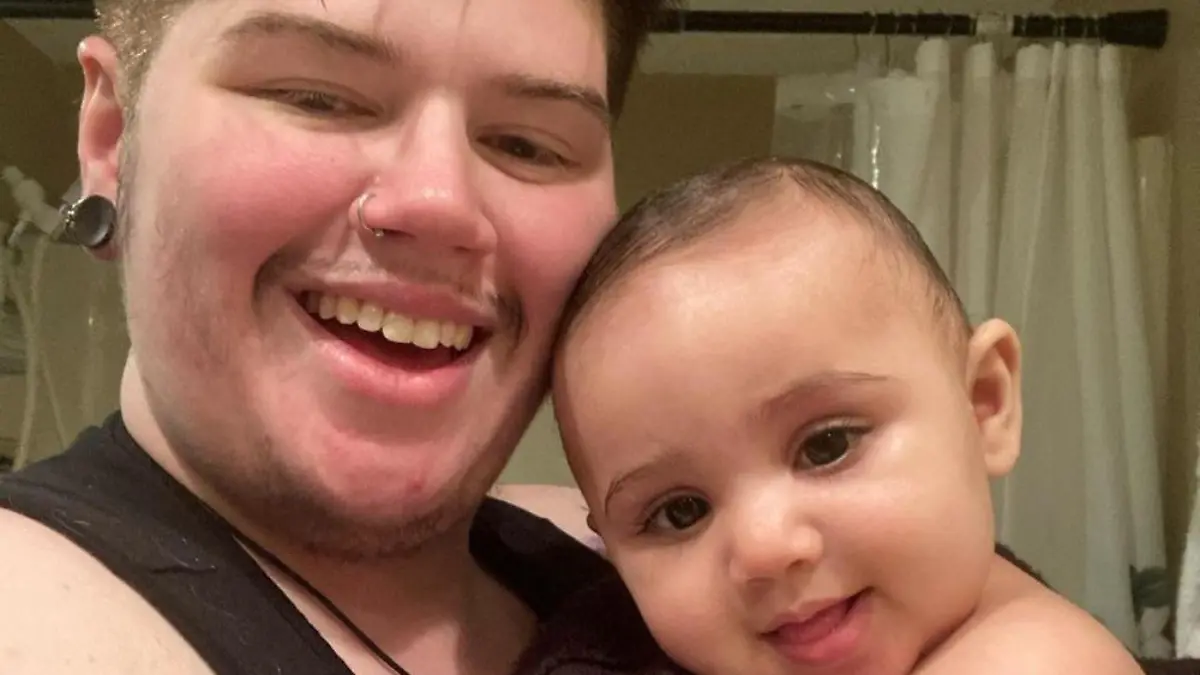 MERCURY PRESS. (Pictured: Ash Patrick Schade, 28, with son Ronan.) A trans man has revealed how he fell pregnant whilst transitioning after a one-night stand. Ash Patrick Schade, 28, had spent the last two years transitioning and taking testosterone and oestrogen blockers when he discovered that he was pregnant in February 2020 after a 'Grindr hook-up'. The mental health worker and PHD student from Huntington, West Virginia, USA was shocked at the revelation, but paused hormone treatments immediately in order to give birth to his daughter, Ronan Shiva, one. SEE MERCURY COPY