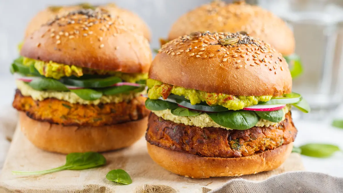 Healthy baked sweet potato burger with whole grain bun, guacamole, vegan mayonnaise and vegetables on a board. Vegetarian food concept, light background.