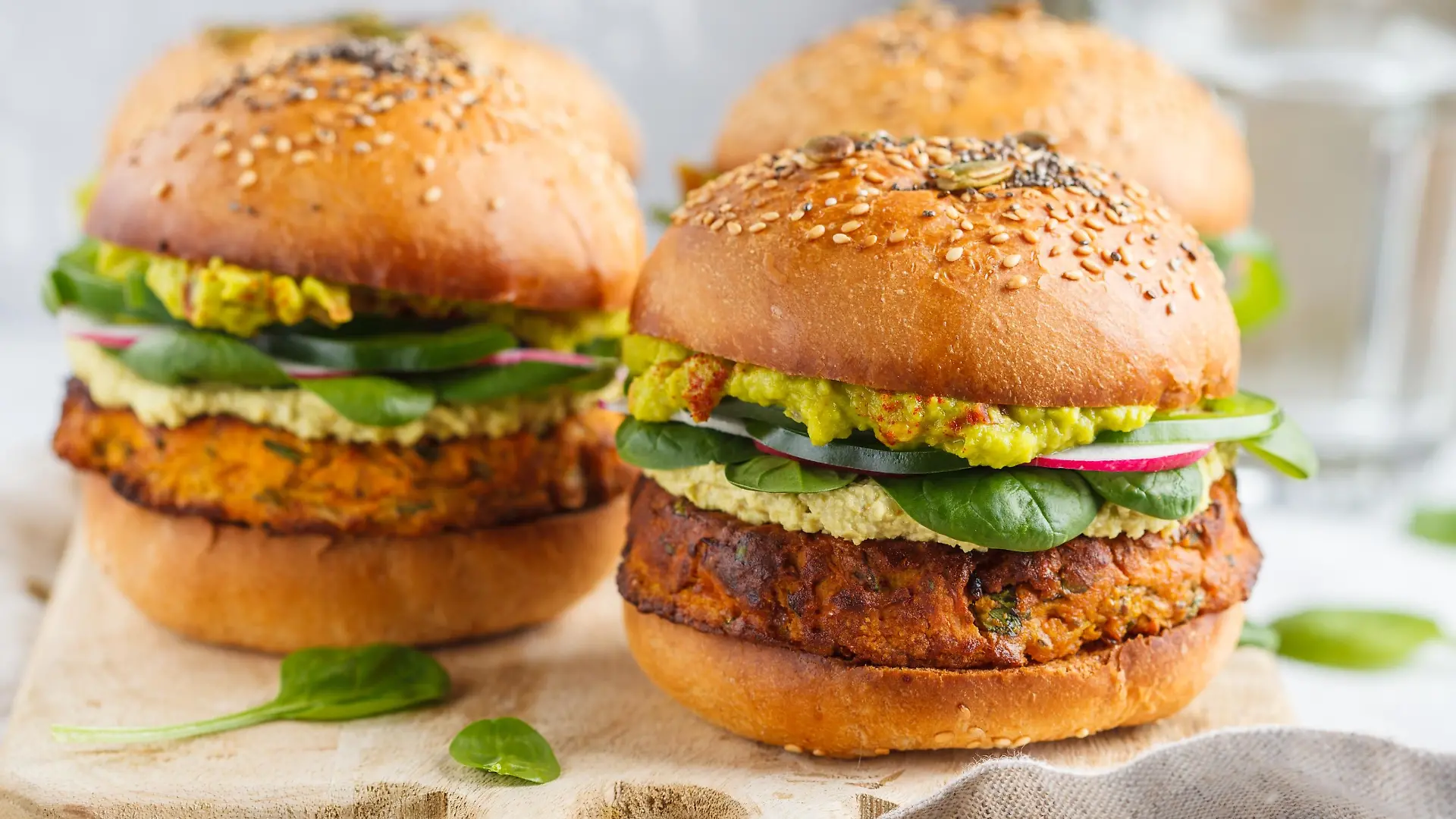 Healthy baked sweet potato burger with whole grain bun, guacamole, vegan mayonnaise and vegetables on a board. Vegetarian food concept, light background.