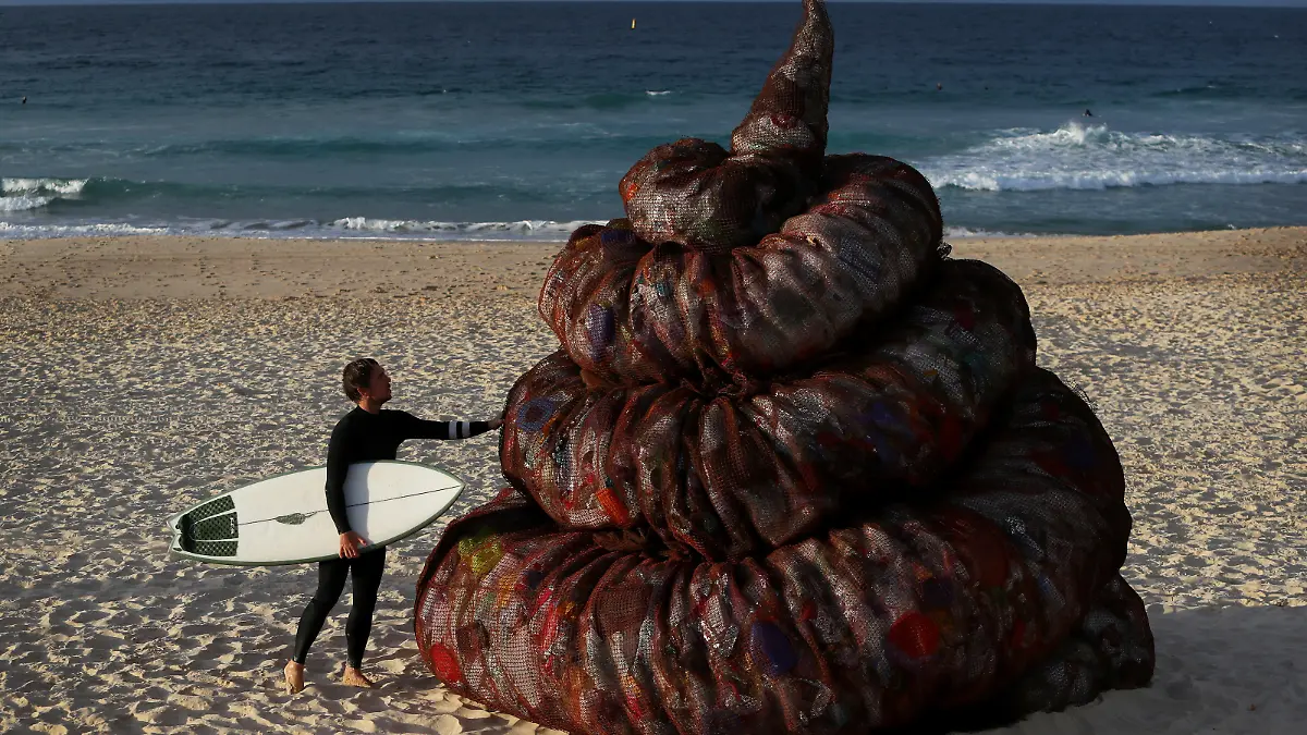 SYDNEY, AUSTRALIA - JUNE 05: A surfer interacts with a sculpture titled 'Plastic pile of sh!t, 2023' presented by Better Packaging Co. at Bondi Beach on June 05, 2023 in Sydney, Australia. The four-metre-high sculpture is made out of recycled plastic and resembles human feces. The sculpture is designed to draw attention to the amount of plastic that's dumped in the world's oceans every 30 seconds. (Photo by Lisa Maree Williams/Getty Images)