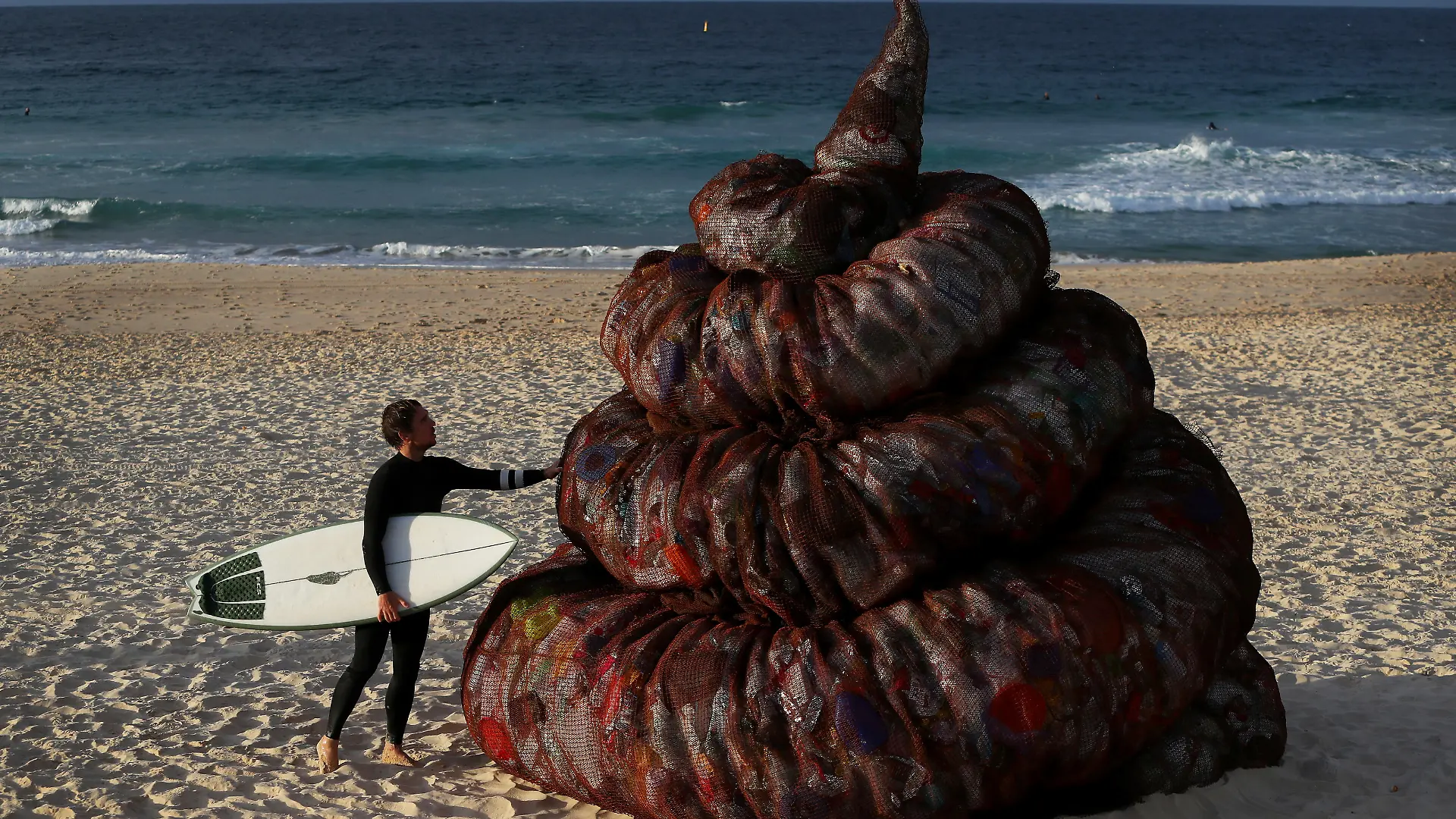 SYDNEY, AUSTRALIA - JUNE 05: A surfer interacts with a sculpture titled 'Plastic pile of sh!t, 2023' presented by Better Packaging Co. at Bondi Beach on June 05, 2023 in Sydney, Australia. The four-metre-high sculpture is made out of recycled plastic and resembles human feces. The sculpture is designed to draw attention to the amount of plastic that's dumped in the world's oceans every 30 seconds. (Photo by Lisa Maree Williams/Getty Images)