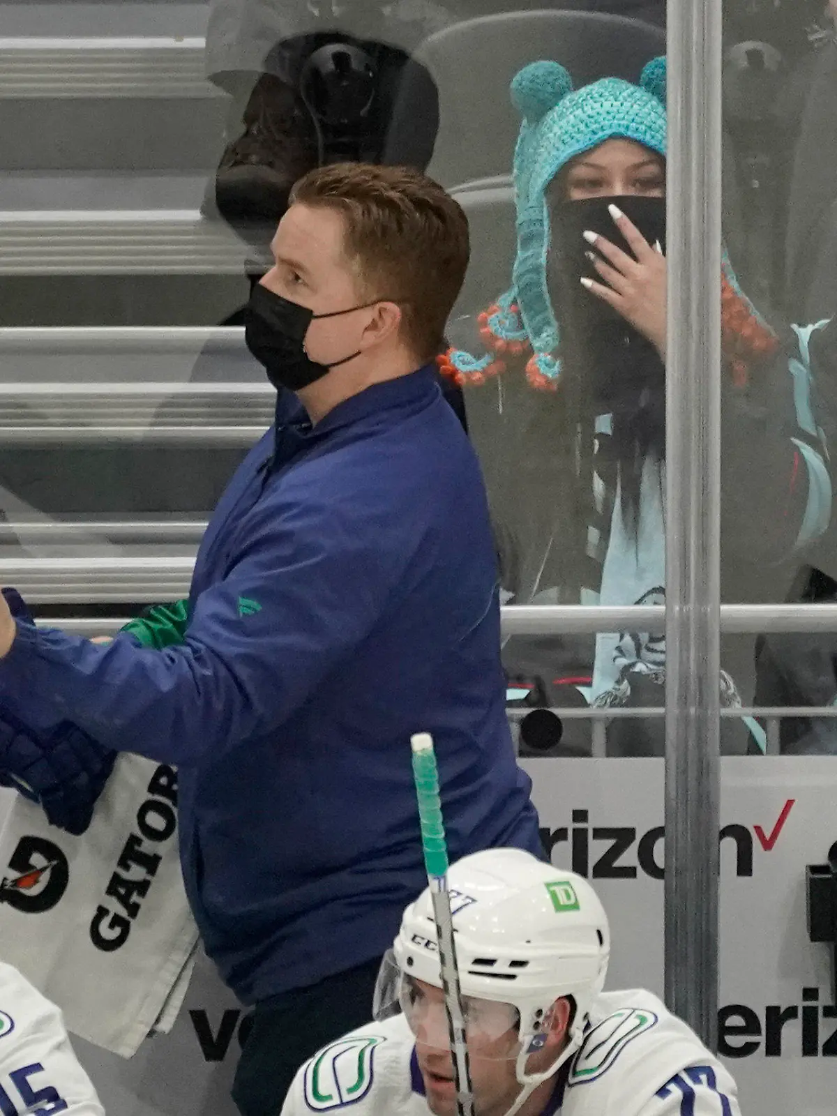 Seattle Kraken fan Nadia Popovici, center, reacts after she was was introduced along with Vancouver Canucks assistant equipment manager Brian "Red" Hamilton, standing, during the first period of an NHL hockey game Saturday, Jan. 1, 2022, in Seattle. During a game between the two teams on Oct. 23, 2021, Popovici showed Hamilton a message on her phone expressing her concern that she believed a mole on the back of Hamilton's neck was cancerous and that he needed to get it checked. A few days later, doctors removed the mole, and biopsy results showed there were cancerous cells in the mole. (AP Photo/Ted S. Warren)