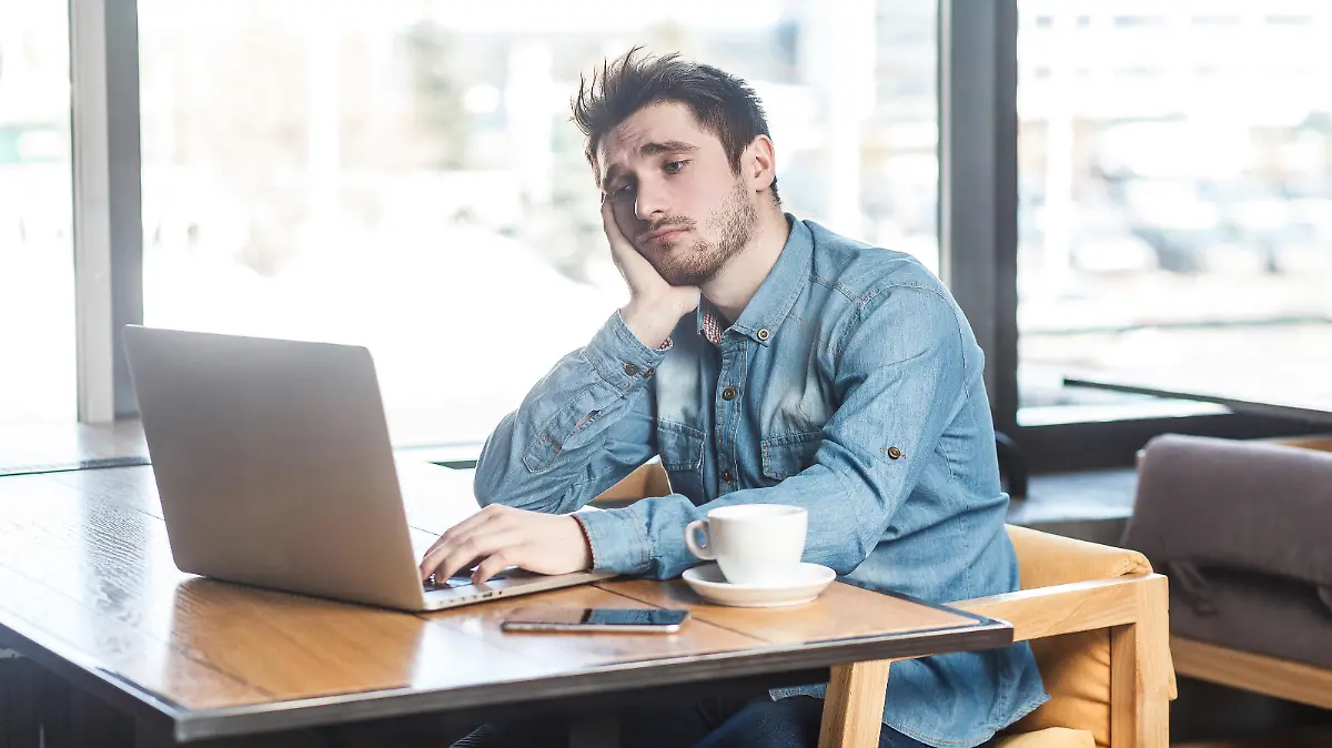 Dont know! Portrait of sadness tired bearded young freelancer in blue jeans shirt are sitting alone in cafe and searching for a work on laptop are in bad mood without good result. || Modellfreigabe vorhanden