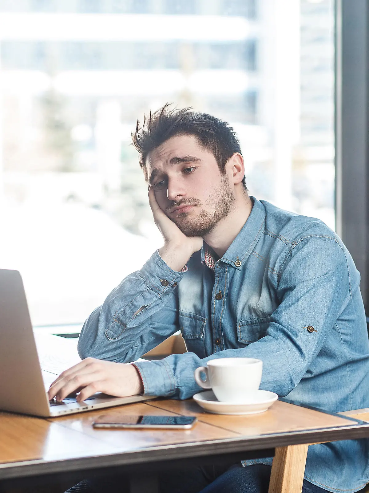 Dont know! Portrait of sadness tired bearded young freelancer in blue jeans shirt are sitting alone in cafe and searching for a work on laptop are in bad mood without good result. || Modellfreigabe vorhanden