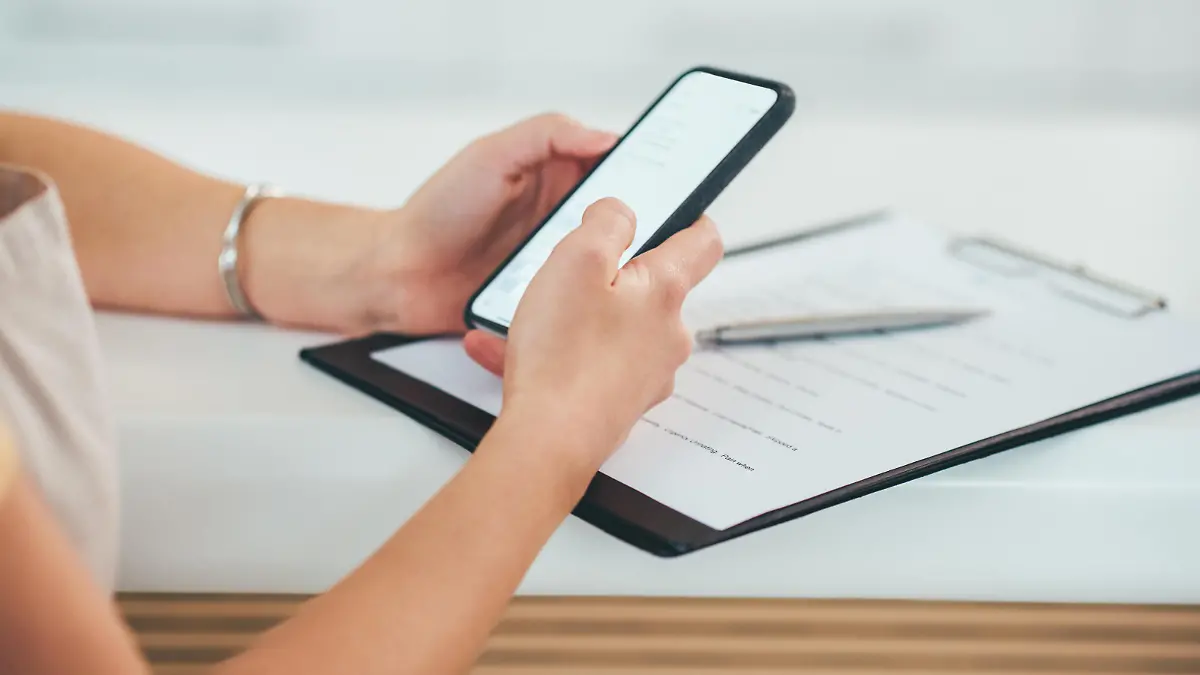 Shot of a woman using a smartphone while going through paperwork in a cafe