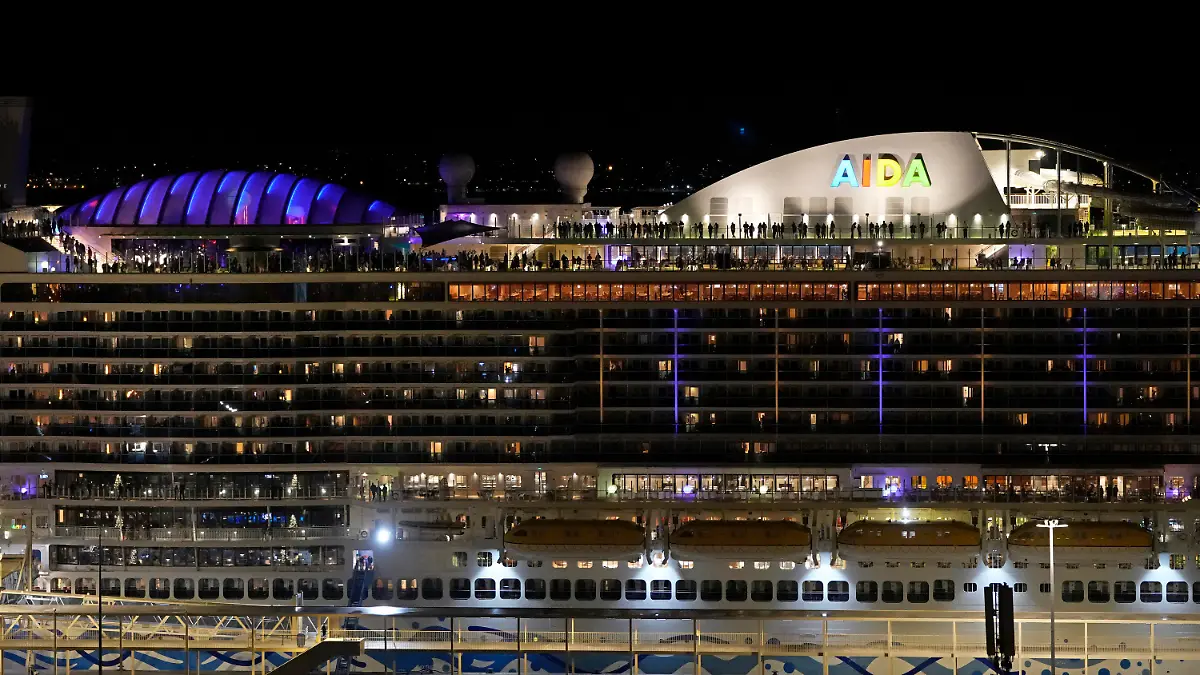 People stand on the deck of the German cruise ship AIDAnova docked in Lisbon, shortly before midnight, Friday, Dec. 31, 2021. According to news reports, the ship, which was on its way to Lanzarote, has been held back in Lisbon due to a coronavirus outbreak aboard. (AP Photo/Armando Franca)