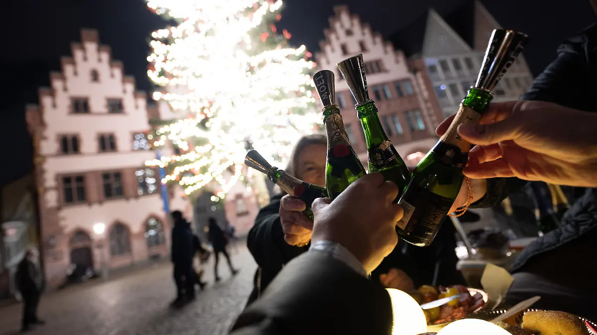 31.12.2021, Hessen, Frankfurt/Main: Menschen stoßen an einem Tisch auf dem Römer mit Champagner an. Aufgrund der Corona-Maßnahmen haben sich die Anstoßenden dazu entschieden an der frischen Luft ins Neue Jahr zu feiern. Vorspeise gab es an der Alten Oper, Hauptgang auf dem Römer und dann das Dessert am Main. Foto: Sebastian Gollnow/dpa +++ dpa-Bildfunk +++