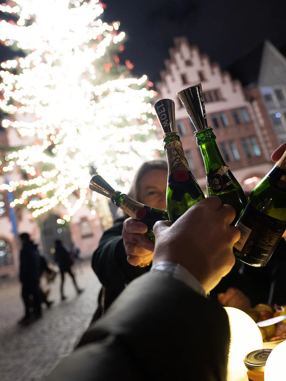 31.12.2021, Hessen, Frankfurt/Main: Menschen stoßen an einem Tisch auf dem Römer mit Champagner an. Aufgrund der Corona-Maßnahmen haben sich die Anstoßenden dazu entschieden an der frischen Luft ins Neue Jahr zu feiern. Vorspeise gab es an der Alten Oper, Hauptgang auf dem Römer und dann das Dessert am Main. Foto: Sebastian Gollnow/dpa +++ dpa-Bildfunk +++