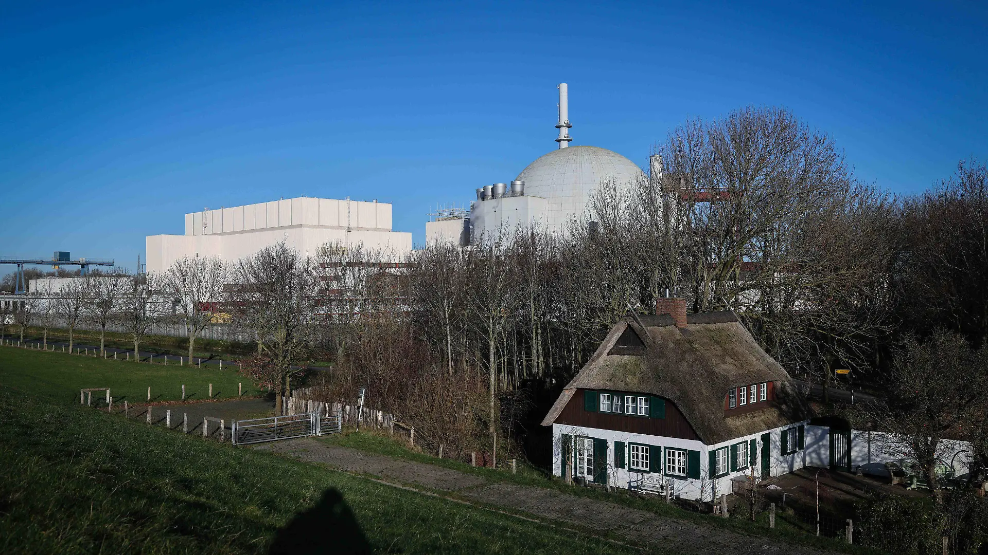 ARCHIV - 20.12.2021, Schleswig-Holstein, Brokdorf: Die Kuppel des Reaktorgebäudes des Kernkraftwerk Brokdorf ist hinter einem Reetdachhaus am Elbdeich zu sehen. (zu dpa «Energiemarktexperte: Märkte sind auf Atom-Abschaltung vorbereitet») Foto: Christian Charisius/dpa +++ dpa-Bildfunk +++