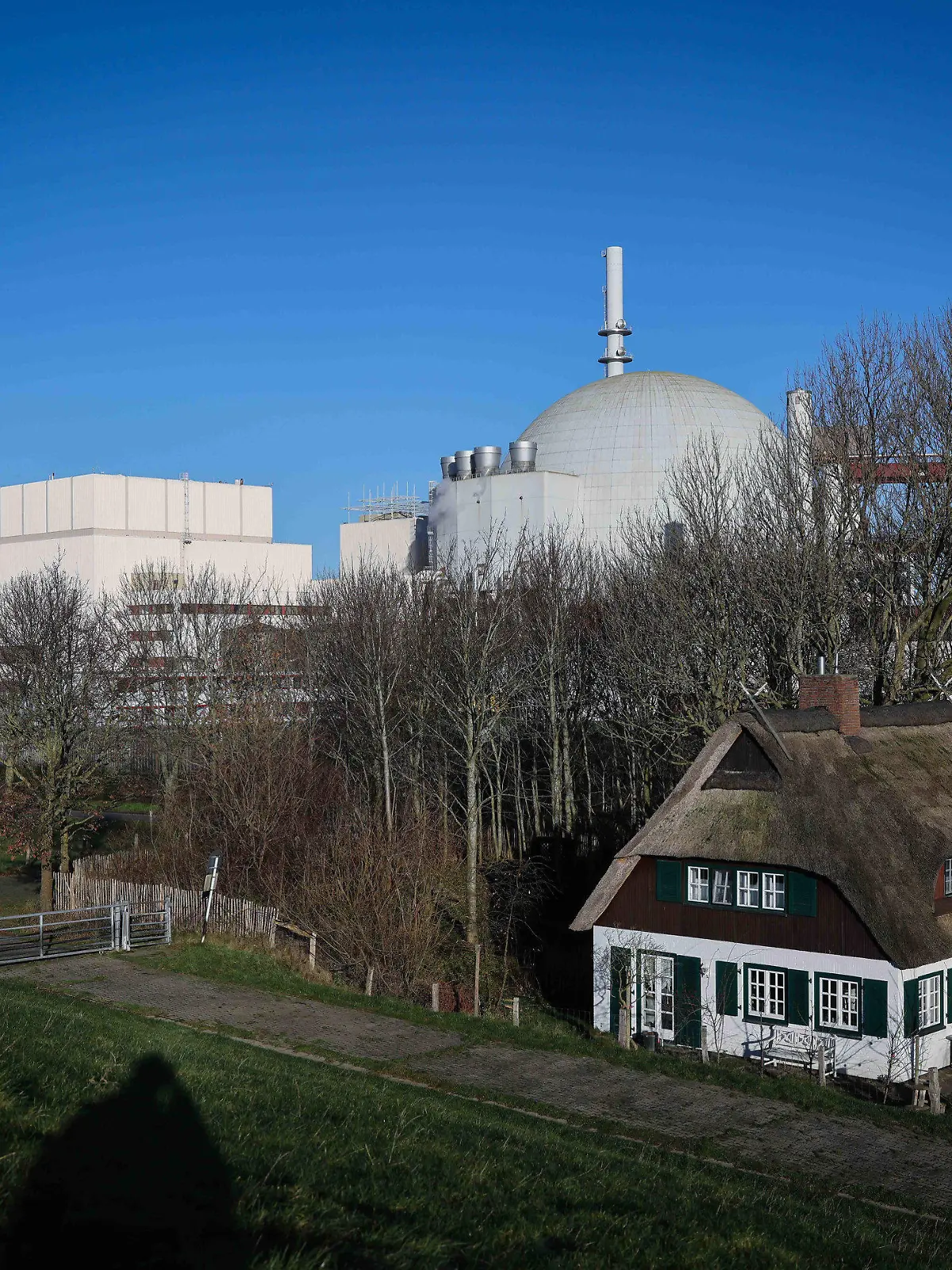 ARCHIV - 20.12.2021, Schleswig-Holstein, Brokdorf: Die Kuppel des Reaktorgebäudes des Kernkraftwerk Brokdorf ist hinter einem Reetdachhaus am Elbdeich zu sehen. (zu dpa «Energiemarktexperte: Märkte sind auf Atom-Abschaltung vorbereitet») Foto: Christian Charisius/dpa +++ dpa-Bildfunk +++