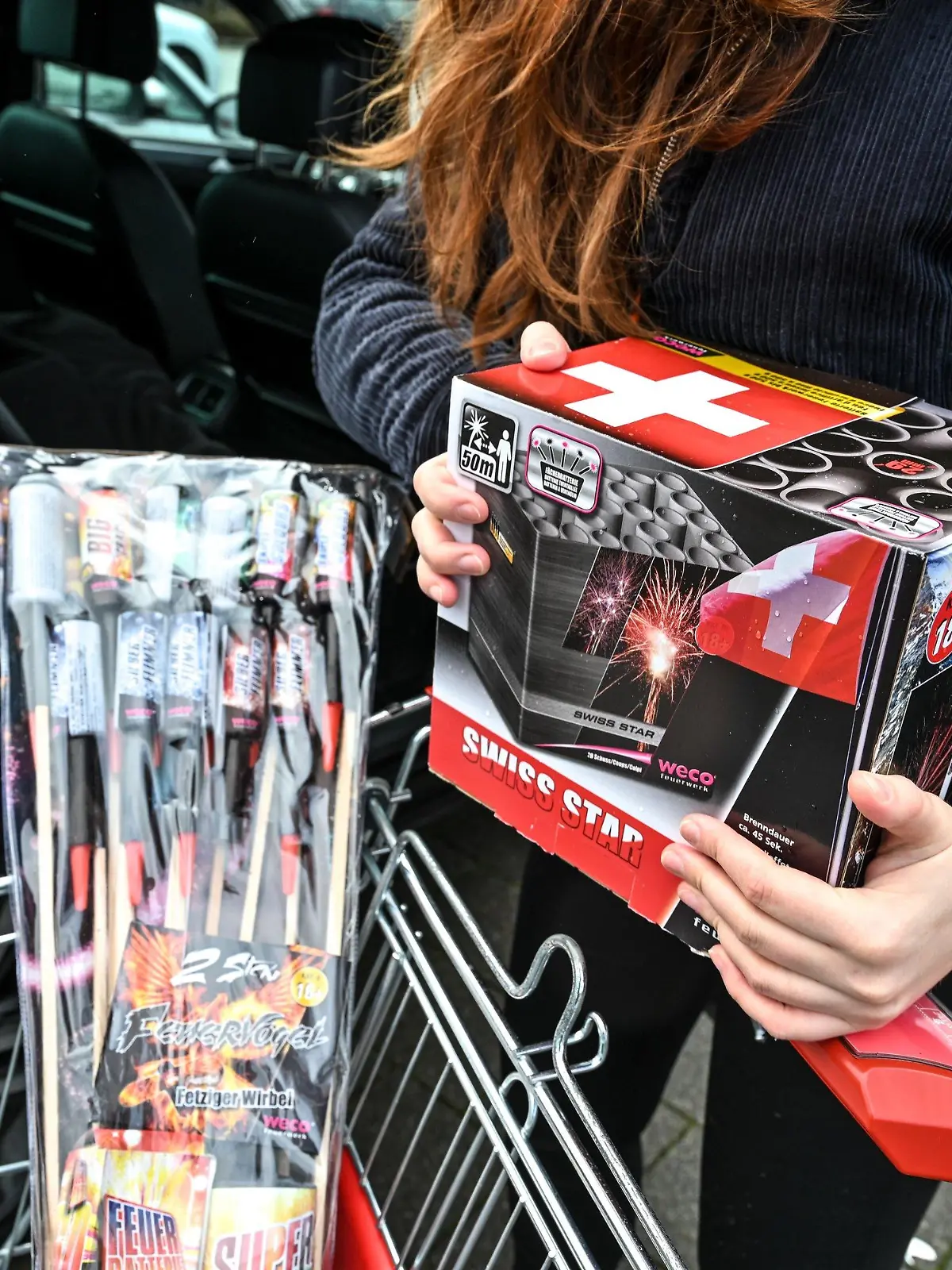 ILLUSTRATION - 27.12.2021, Schweiz, Kreuzlingen: Die Konstanzerin Leonie hält eine Packung Feuerwerkskörper in den Armen, um sie dann auf die Rückbank eines Autos zu legen. (gestellte Aufnahmesituation) Foto: Felix Kästle/dpa +++ dpa-Bildfunk +++