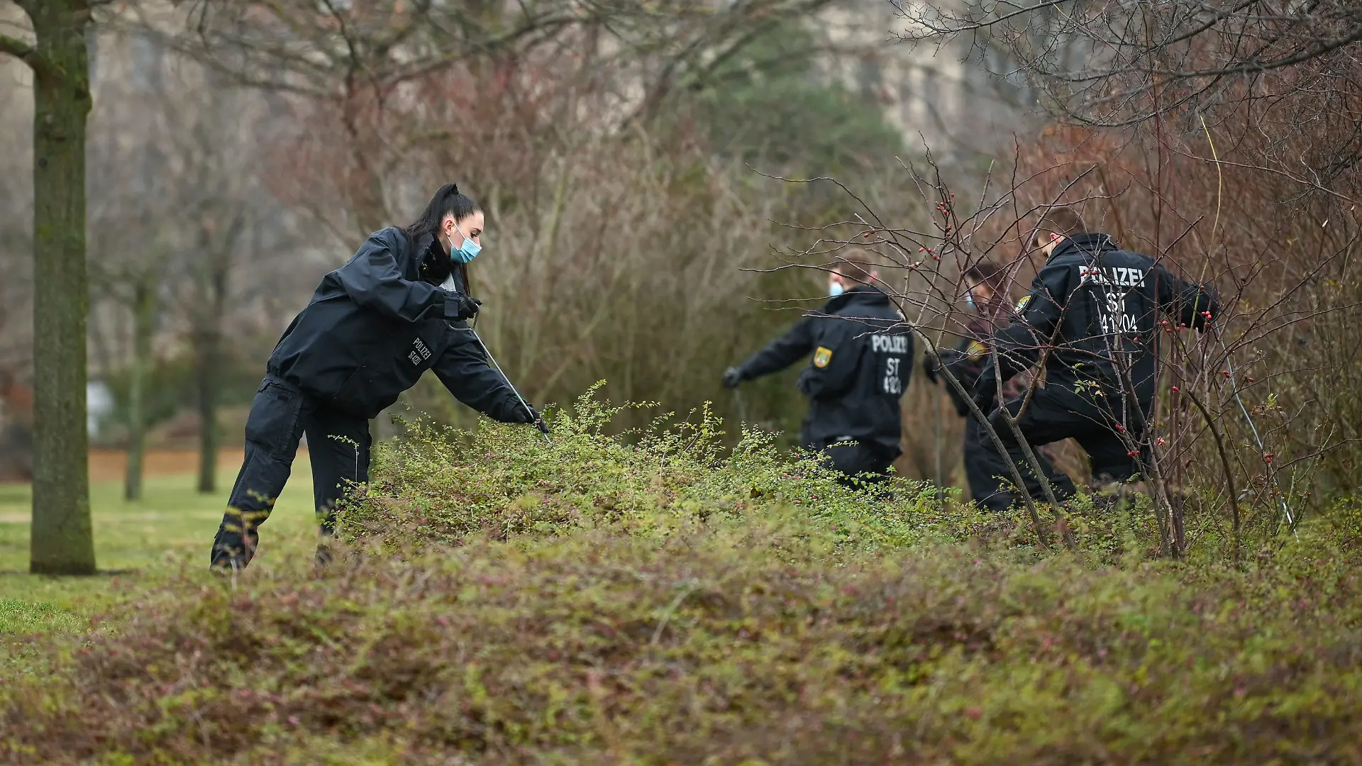 28.12.2021, Sachsen-Anhalt, Halle (Saale): Eine Polizistin durchsucht zusammen mit Kollegen ein Gebüsch. Am Zaun der Halleschen Stadtwirtschaft wurde am Abend zuvor eine Babyleiche gefunden. Die Kriminalpolizei sicherte vor Ort umfangreiche Spuren. Foto: Heiko Rebsch/dpa-Zentralbild/dpa +++ dpa-Bildfunk +++