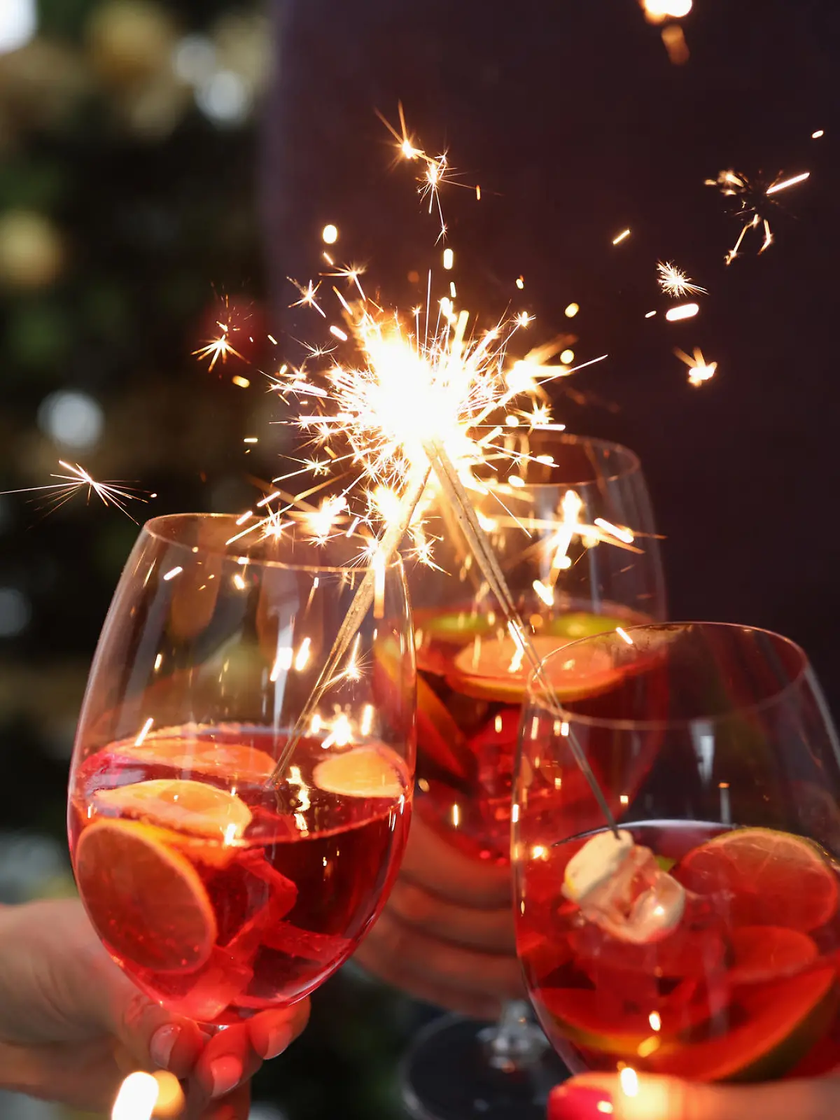 Group of people holding glasses with cocktails and sparklers closeup. New Years and Christmas celebrations concept