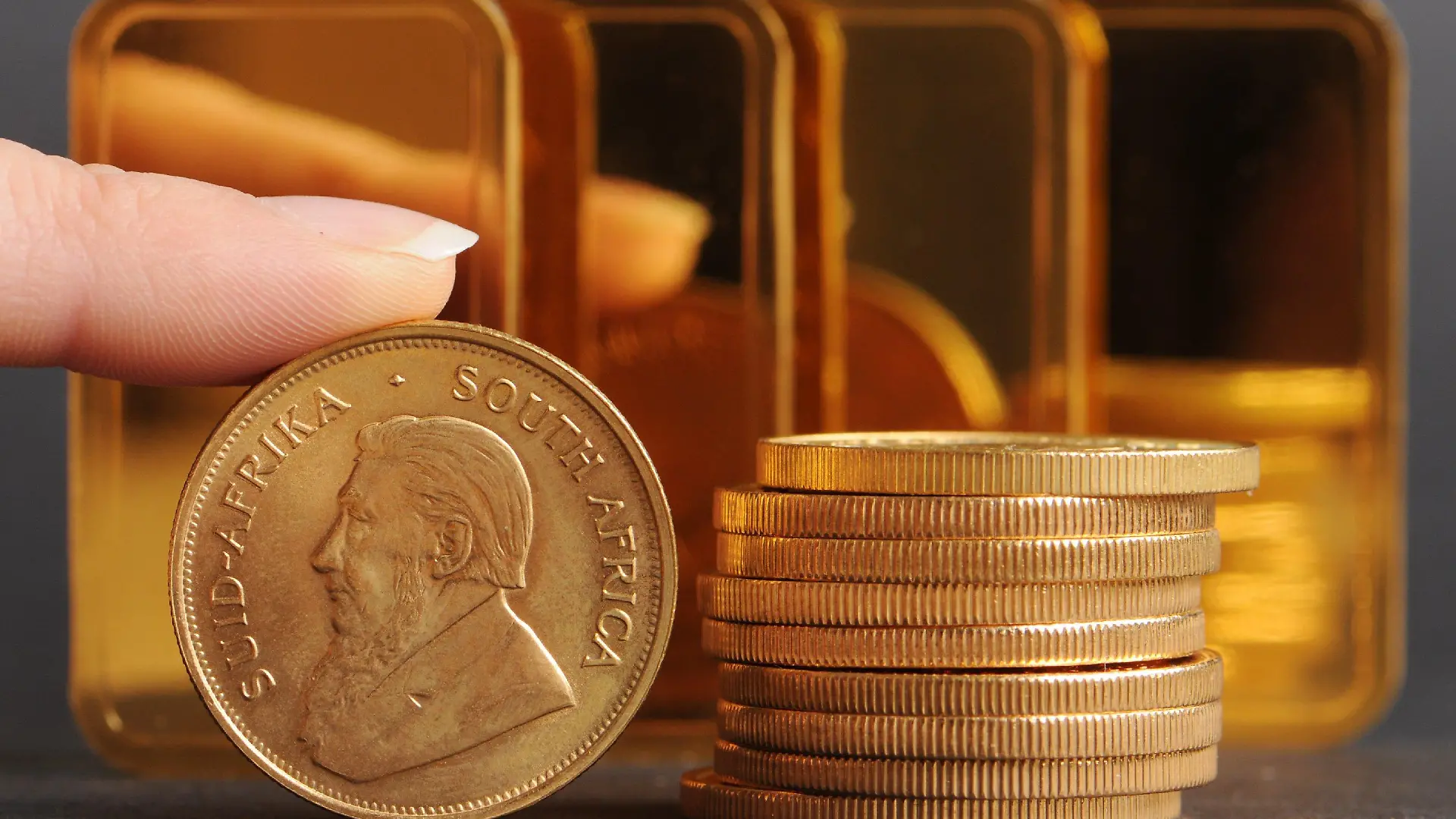 Ein Finger hält am Donnerstag (20.03.2008) in Straubing (Niederbayern) eine südafrikanischen Krügerrand-Münze vor Goldbarren (100 Gramm). Der Preis für eine Feinunze Gold (31,1 Gramm) war am Montag auf den Rekord von 1032,50 Dollar hochgeschossen. Foto: Armin Weigel dpa/lby +++(c) dpa - Bildfunk+++