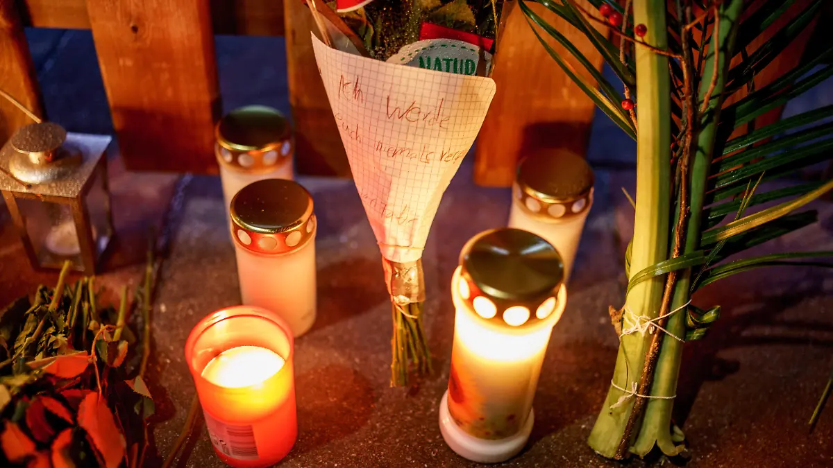 27.12.2021, Schleswig-Holstein, Glinde: Kerzen, Blumen und ein Blumenstrauß mit einem Zettel mit der Aufschrift ·ich werde Euch niemals vergessen·, stehen vor dem Eingang zu einem Haus, in dem am zweiten Weihnachtstag drei Menschen einer vierköpfigen Familie tot gefunden wurden. Es handelt sich um Kinder im Alter von 11 und 13 Jahren sowie einen Mann, alle mit Schussverletzungen, wie Polizei und Staatsanwaltschaft am Montagvormittag mitteilten. Foto: Axel Heimken/dpa +++ dpa-Bildfunk +++