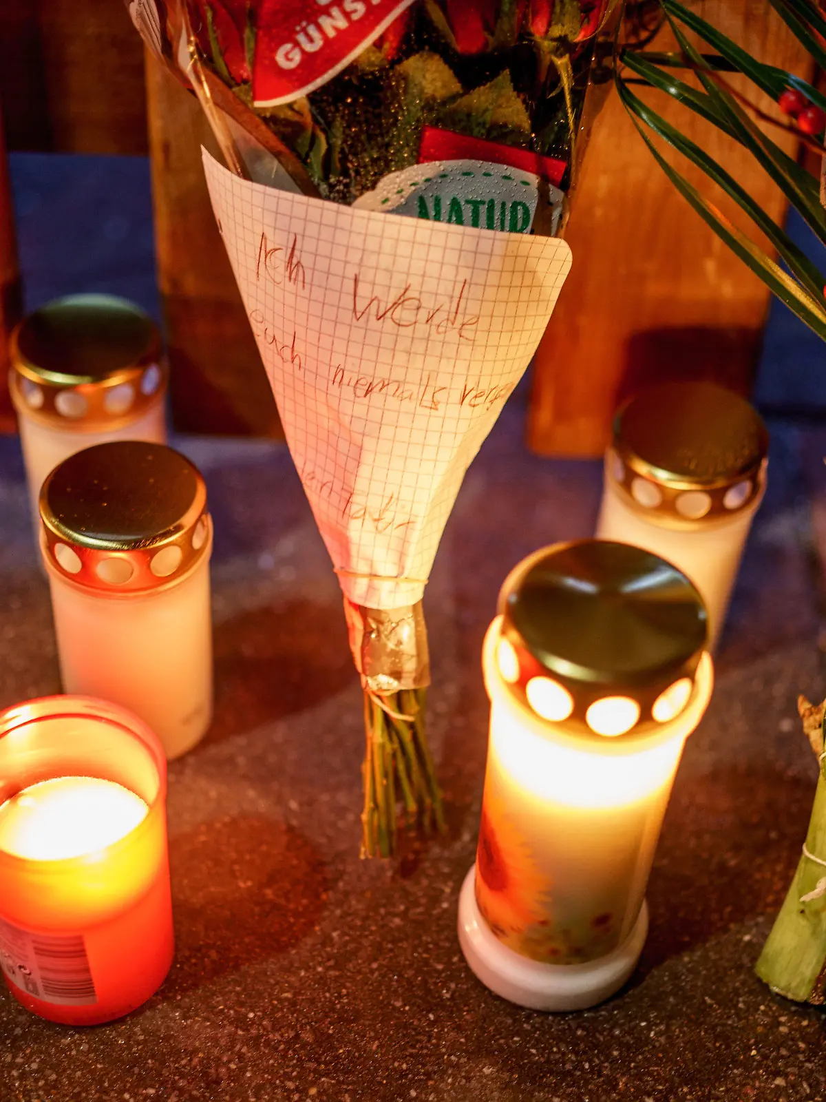 27.12.2021, Schleswig-Holstein, Glinde: Kerzen, Blumen und ein Blumenstrauß mit einem Zettel mit der Aufschrift ·ich werde Euch niemals vergessen·, stehen vor dem Eingang zu einem Haus, in dem am zweiten Weihnachtstag drei Menschen einer vierköpfigen Familie tot gefunden wurden. Es handelt sich um Kinder im Alter von 11 und 13 Jahren sowie einen Mann, alle mit Schussverletzungen, wie Polizei und Staatsanwaltschaft am Montagvormittag mitteilten. Foto: Axel Heimken/dpa +++ dpa-Bildfunk +++