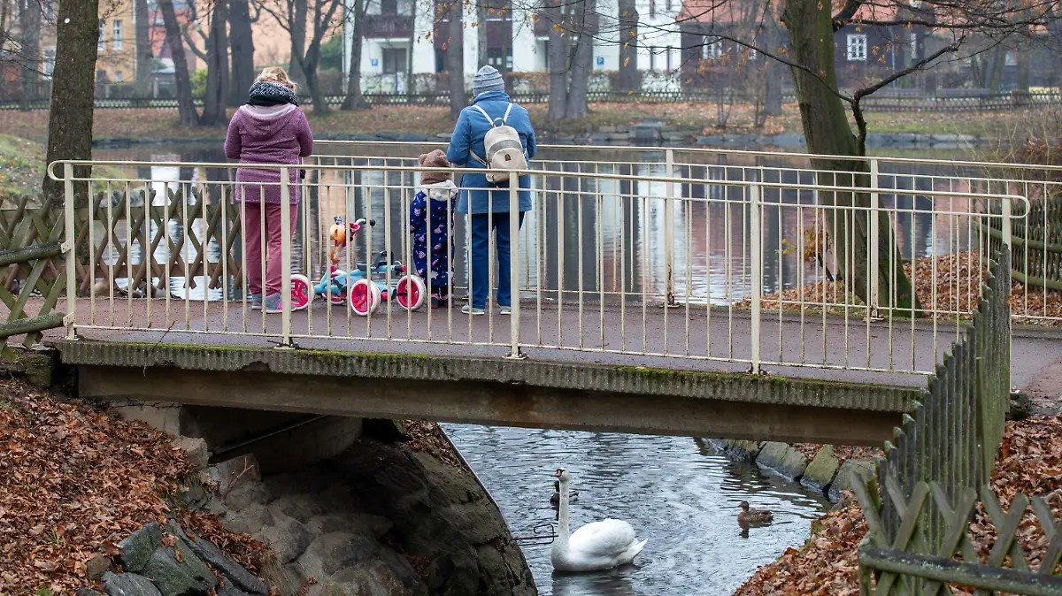 28.11.2021, Sachsen, Neustadt in Sachsen: Zwei Frauen stehen zusammen mit einem kleinen Kind auf einer Brücke im Arthur-Richter-Park in Neustadt und füttern Enten und einen Schwan. In Sachsen war für das Wochenende Schnee angekündigt, doch es wurde vielerorts nur Nebel daraus. Foto: Daniel Schäfer/dpa-Zentralbild/dpa +++ dpa-Bildfunk +++