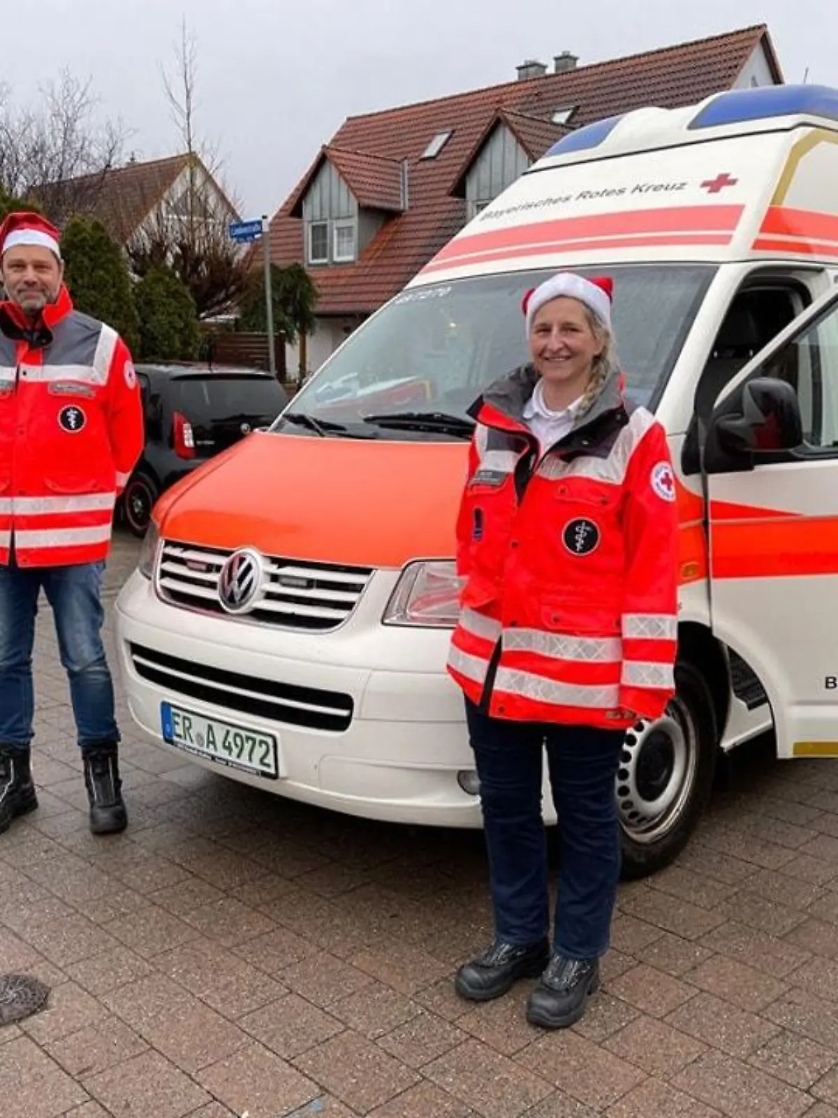 Zwei Mitarbeiter des Roten Kreuzes stehen mit Weihnachtsmütze vor einem Rettungswagen.