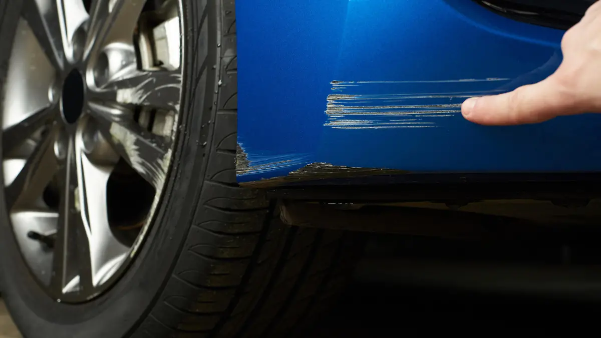 Finger zeigt auf Kratzer am Auto