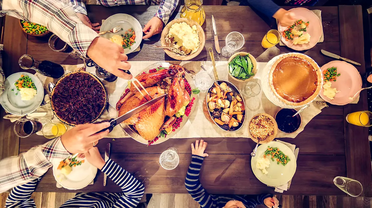 Family having traditional holiday dinner with stuffed turkey, mashed potatoes, cranberry sauce, vegetables pumpkin and pecan pie.