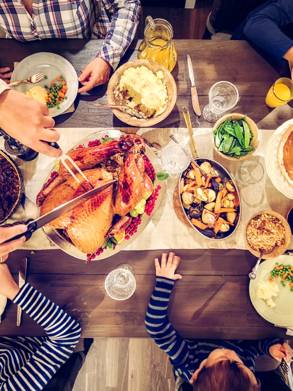 Family having traditional holiday dinner with stuffed turkey, mashed potatoes, cranberry sauce, vegetables pumpkin and pecan pie.