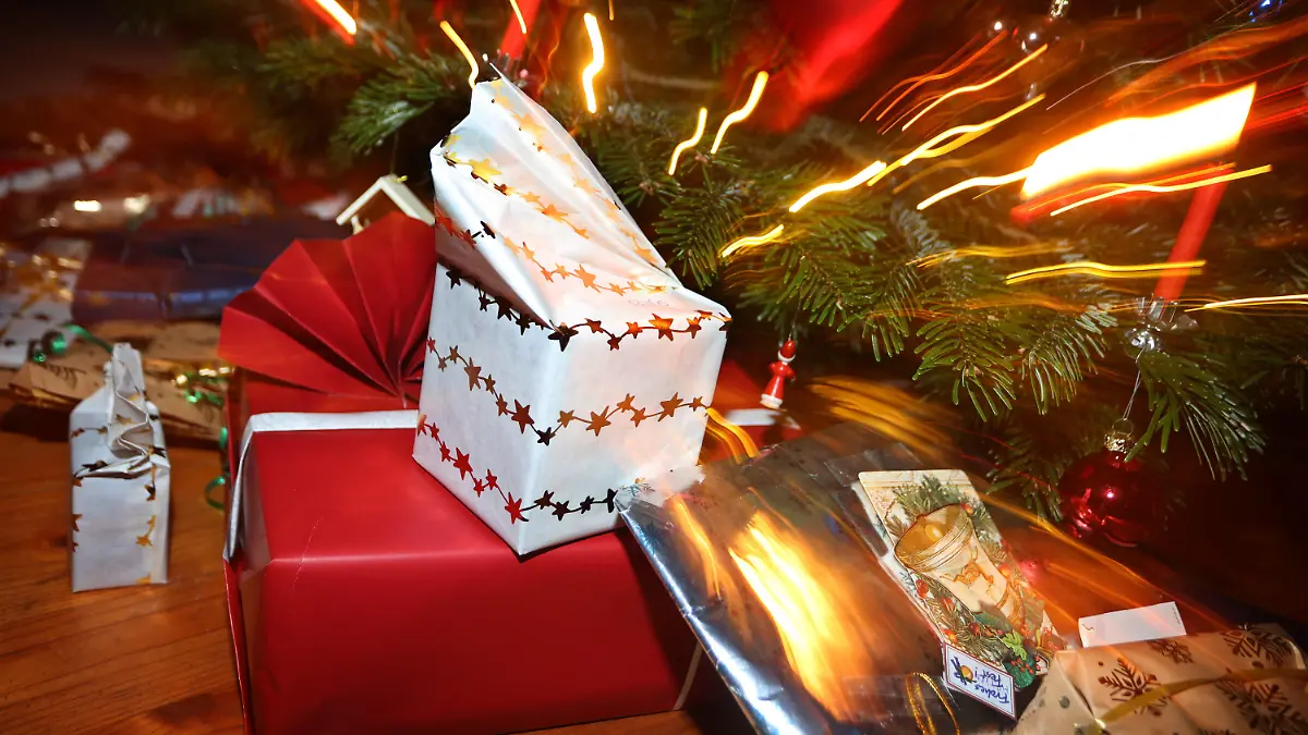 24.12.2021, Bayern, Kaufbeuren: Verpackte Geschenke liegen in einem Wohnzimmer unter einem festlich geschmücktem Weihnachtsbaum. Foto: Karl-Josef Hildenbrand/dpa +++ dpa-Bildfunk +++