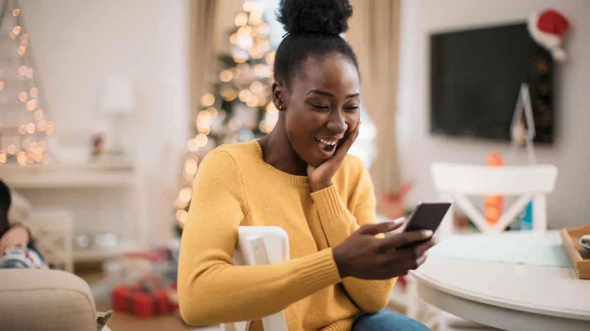 Happy young African American woman using a smart phone, staying in touch with her family and friends and wishing them a Marry Christmas and a happy new year