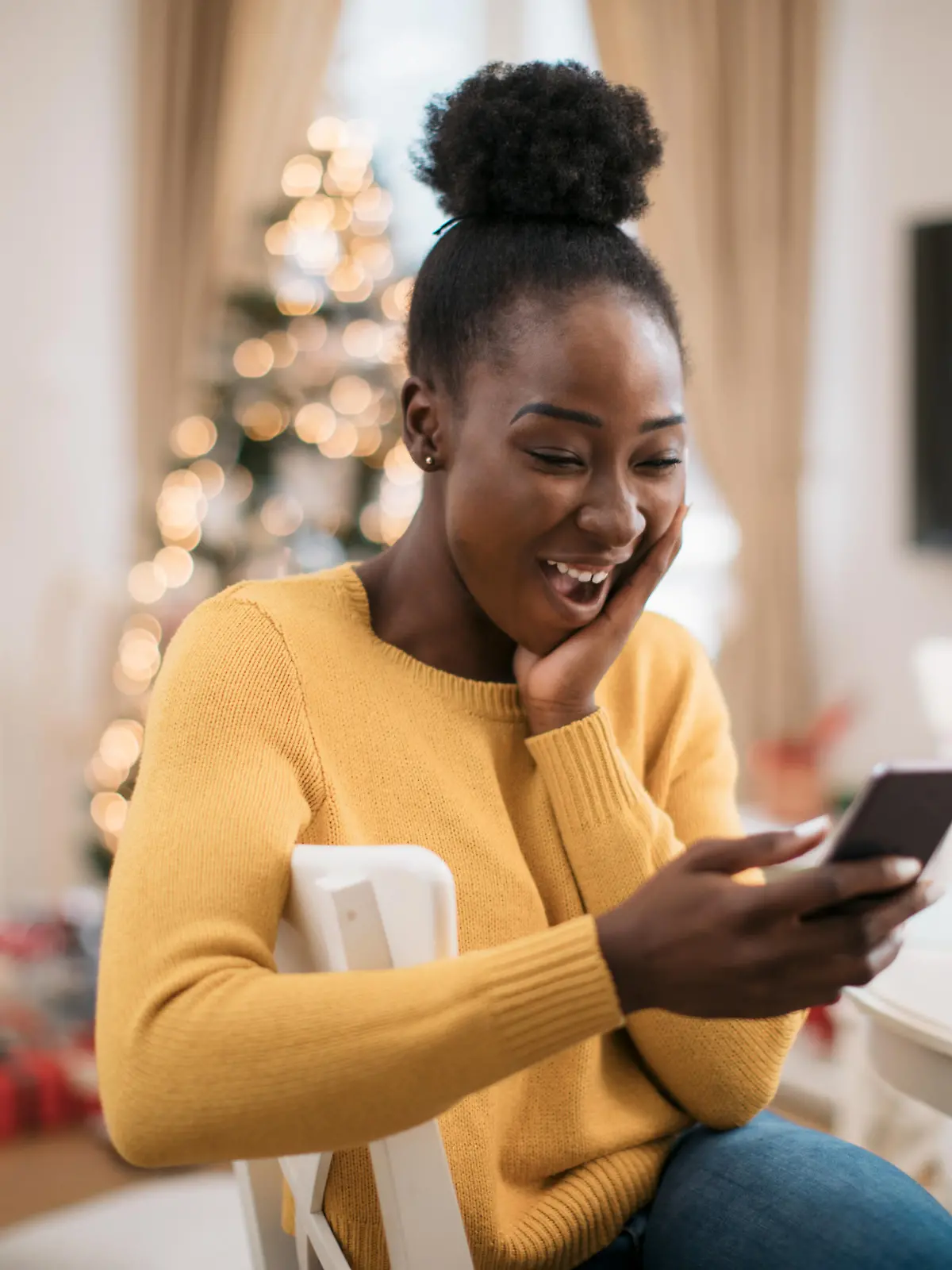 Happy young African American woman using a smart phone, staying in touch with her family and friends and wishing them a Marry Christmas and a happy new year