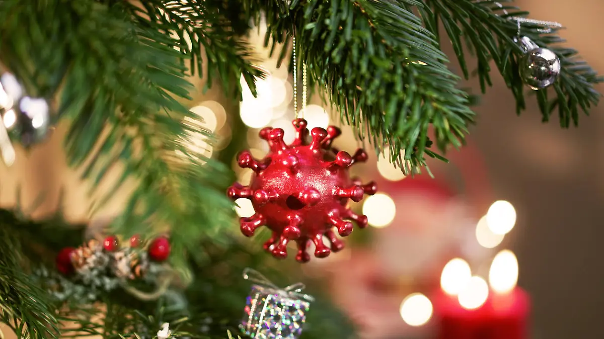 A Christmas Ball hanging on a decorated christmastree with candels in the background. The Christmas Ball is shaped like a Corona virus.