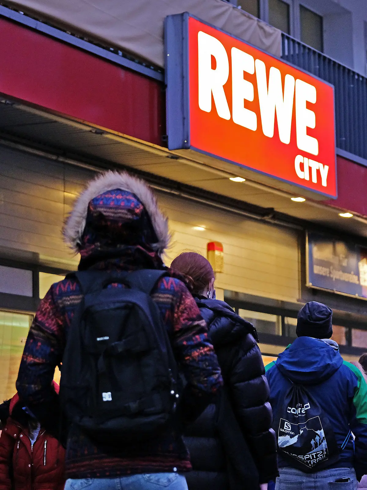 25.11.2020, Nordrhein-Westfalen, Köln: Menschen stehen vor einem Rewe-Supermarkt in einer Schlange an, da sich aufgrund von Corona-Beschränkungen nur eine bestimmte Anzahl von Kunden gleichzeitig im Laden aufhalten darf. Die Länder fordern vor den Beratungen mit mit Kanzlerin Merkel strengere Kontaktbeschränkungen, um die die hohen Coronazahlen zu senken. Für Weihnachten und Silvester sollen Sonderregeln gelten. Foto: Oliver Berg/dpa +++ dpa-Bildfunk +++