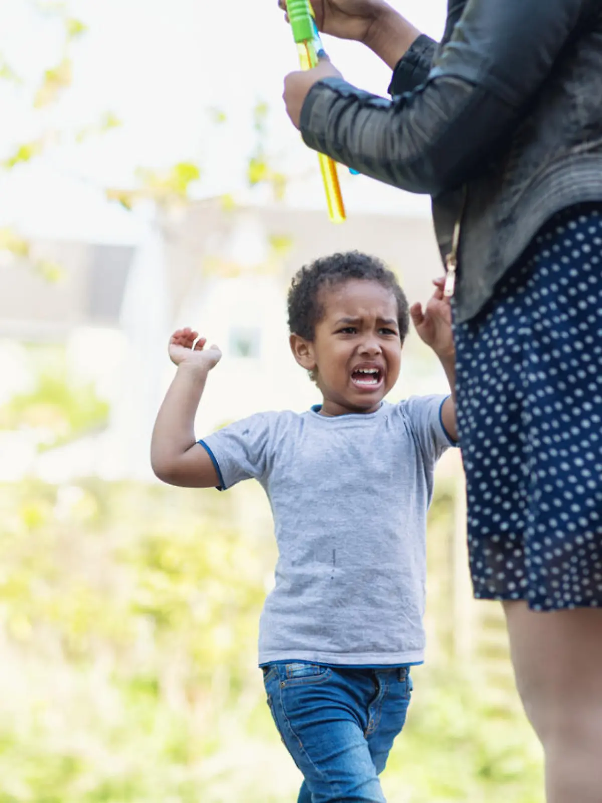 afro american toddler boy, 3 years old, screaming ad crying, diappointed about something his mother will not do. Mother is there too, but focus is on the boy. They are outdoors in backyard, it is summer