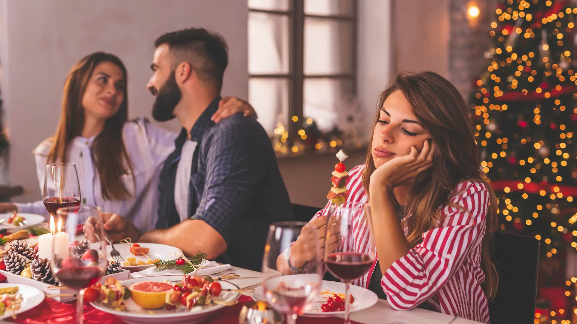 Lonely woman spending Christmas Eve with friends at home, sad while sitting over Christmas dinner surrounded with couples in love