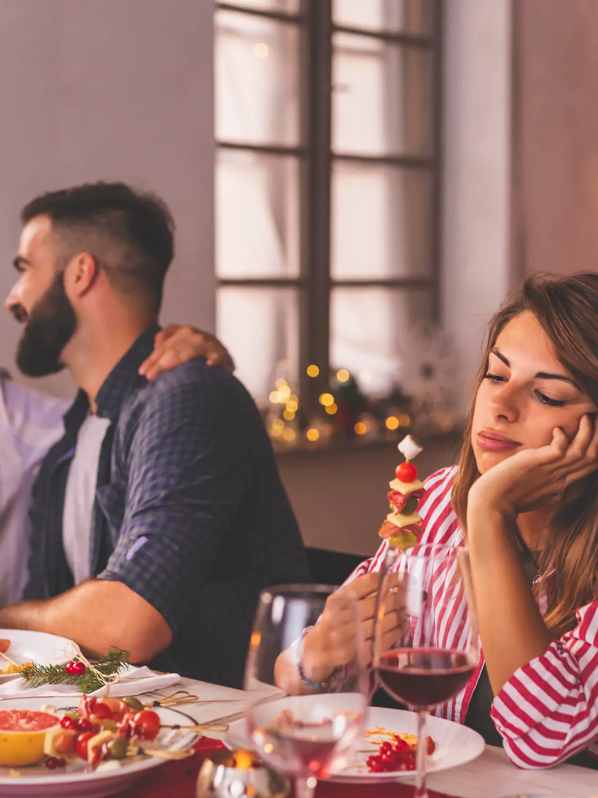 Lonely woman spending Christmas Eve with friends at home, sad while sitting over Christmas dinner surrounded with couples in love