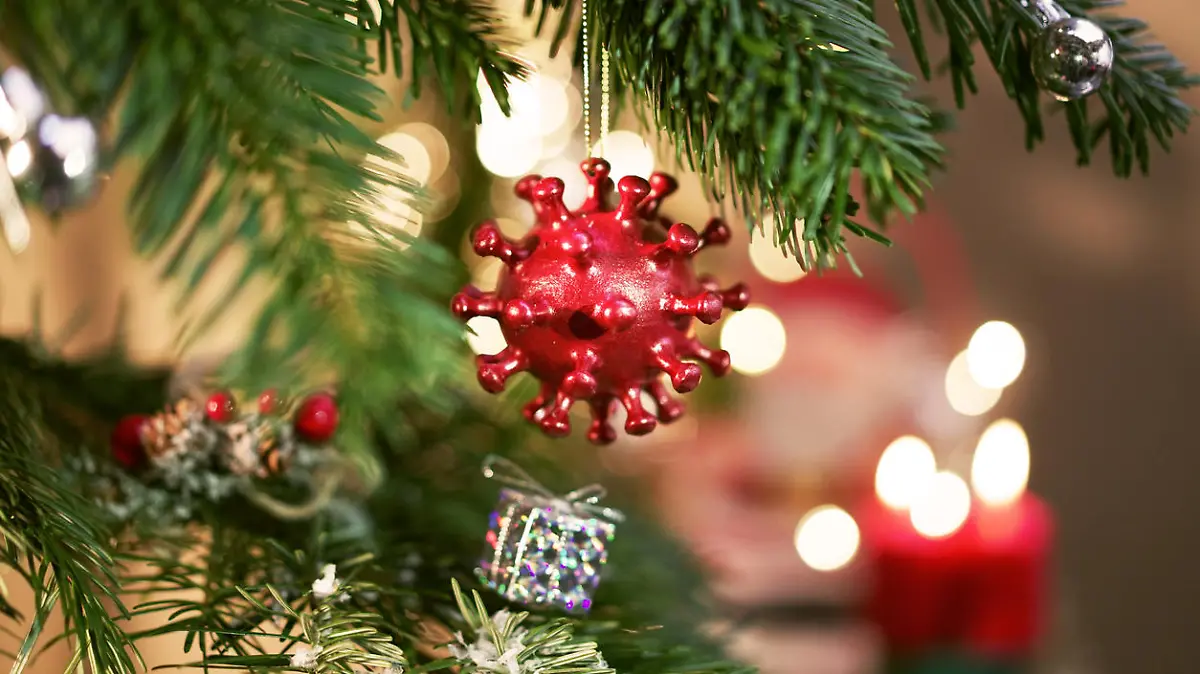 A Christmas Ball hanging on a decorated christmastree with candels in the background. The Christmas Ball is shaped like a Corona virus.