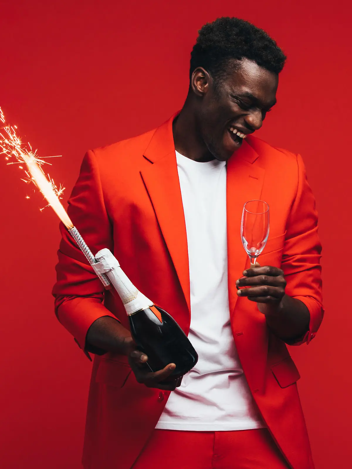 African man celebrating new years with champagne and firework. Stylish guy having fun against red background.