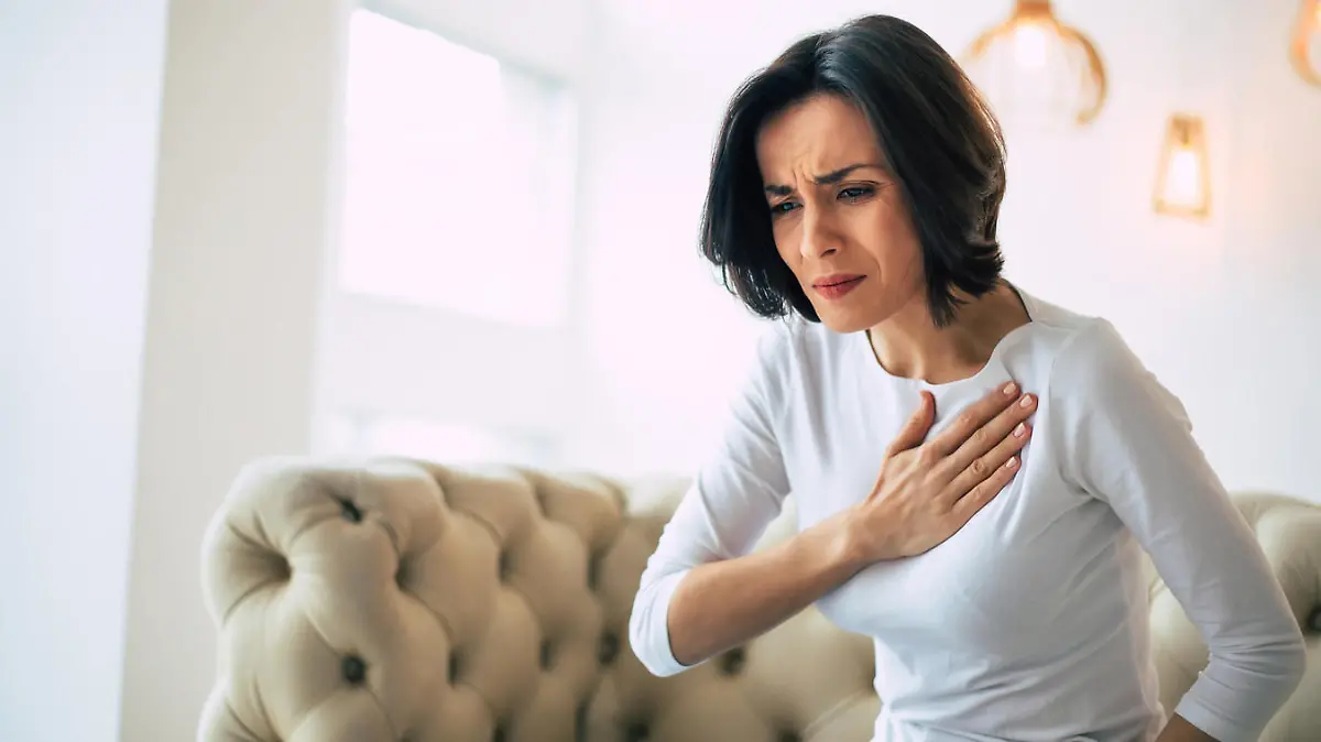 A stressed woman who is suffering from a chest pain and touching her heart area.
