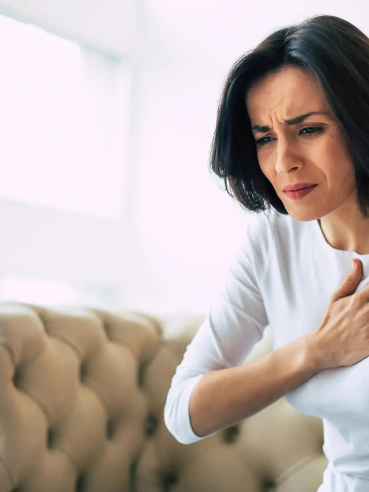 A stressed woman who is suffering from a chest pain and touching her heart area.