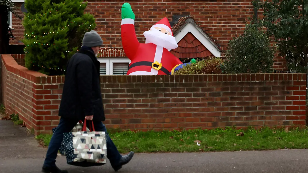 A man carrying shopping bags walks past a partially deflated blow-up Santa Claus amid the coronavirus disease (COVID-19) pandemic, in London, Britain December 20, 2021. REUTERS/Kevin Coombs