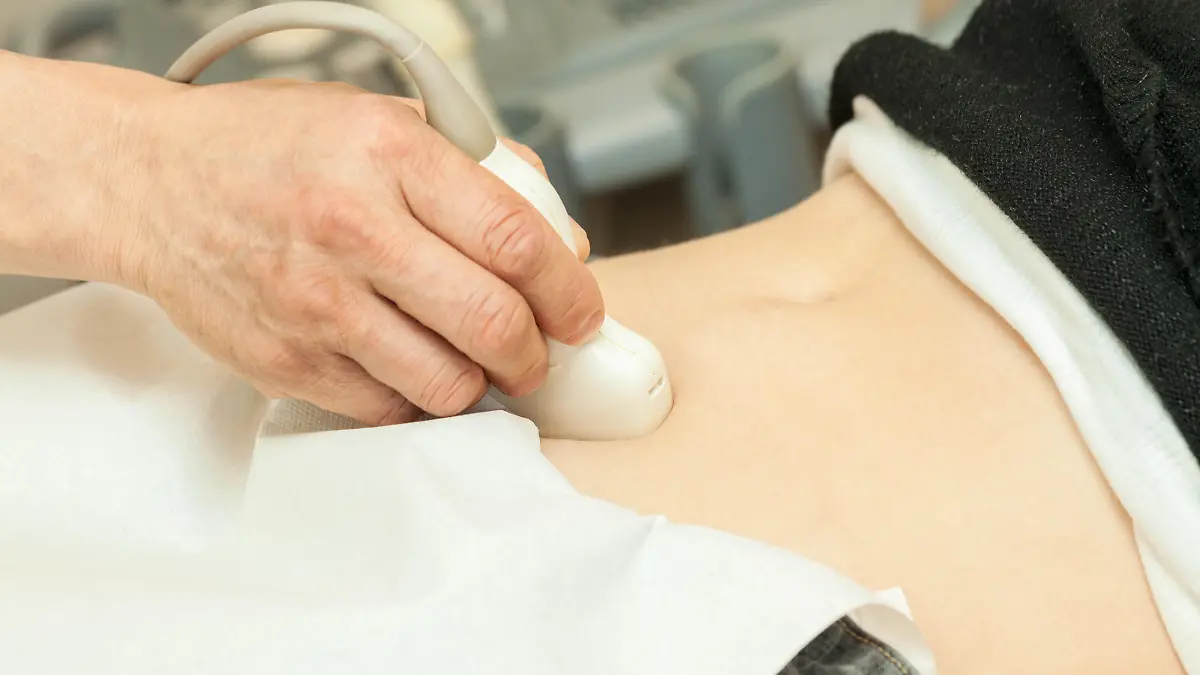 Image of mid adult woman having abdominal ultrasound. Close up of her belly with doctor's hand and ultrasound. selective focus.