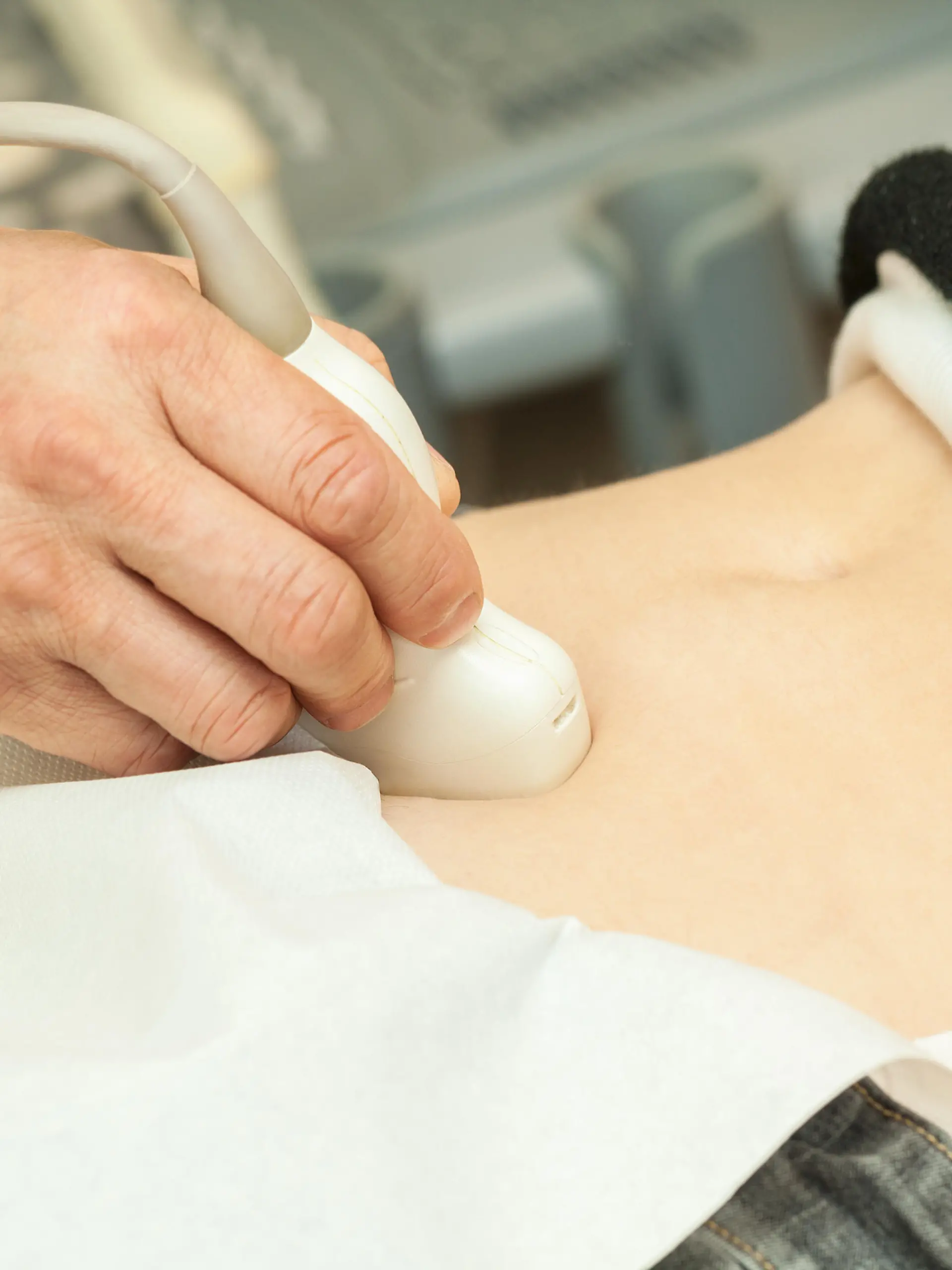 Image of mid adult woman having abdominal ultrasound. Close up of her belly with doctor's hand and ultrasound. selective focus.