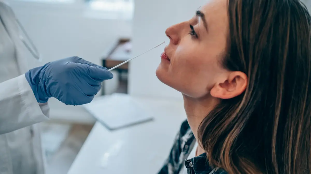 Shot of a doctor using cotton swab while doing coronavirus PCR test at the hospital. Doctor laboratory assistant takes swab from nose of sick patient. Unrecognizable doctor with protective glove taking coronavirus sample from female patient's nose.