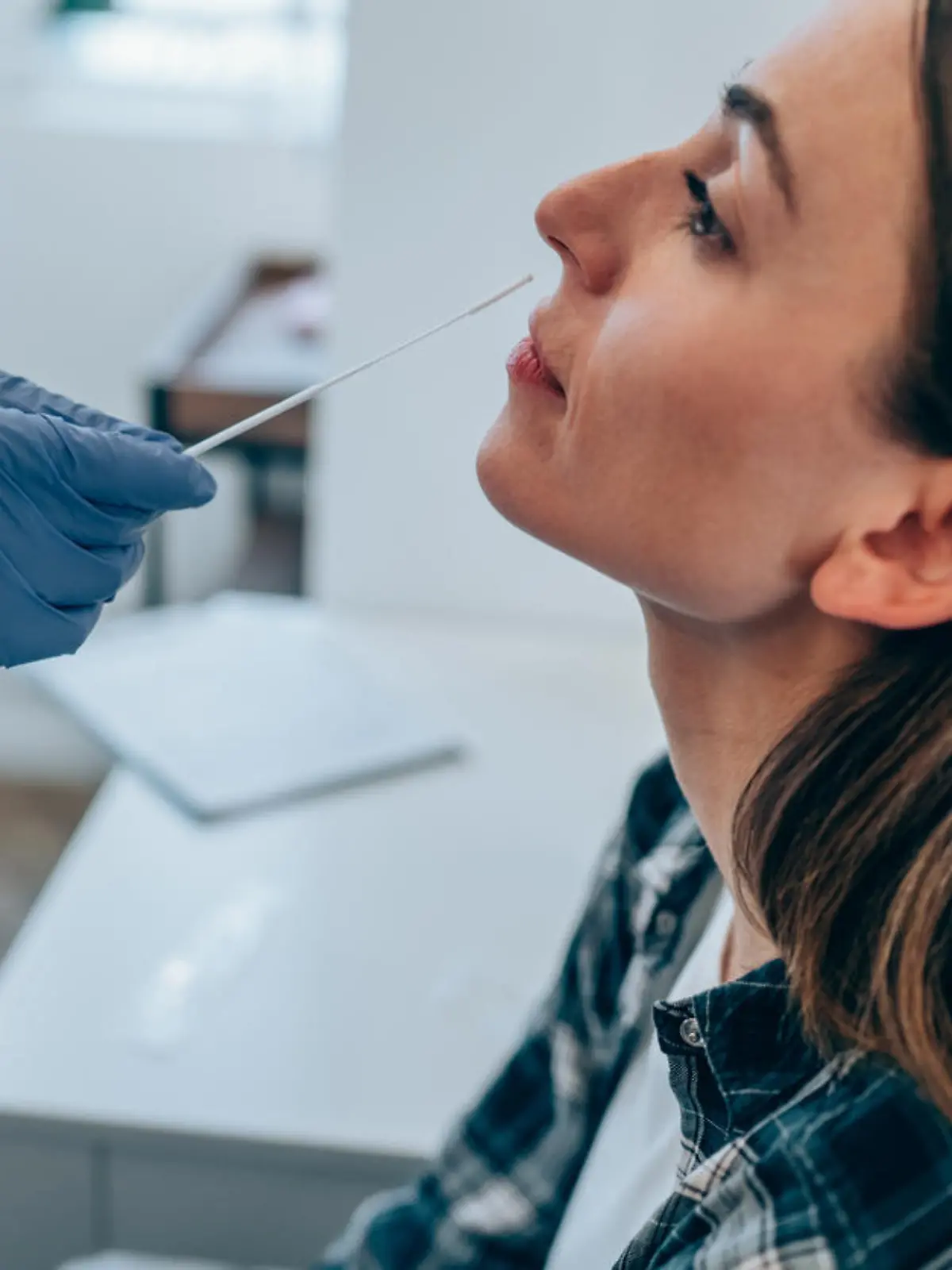 Shot of a doctor using cotton swab while doing coronavirus PCR test at the hospital. Doctor laboratory assistant takes swab from nose of sick patient. Unrecognizable doctor with protective glove taking coronavirus sample from female patient's nose.