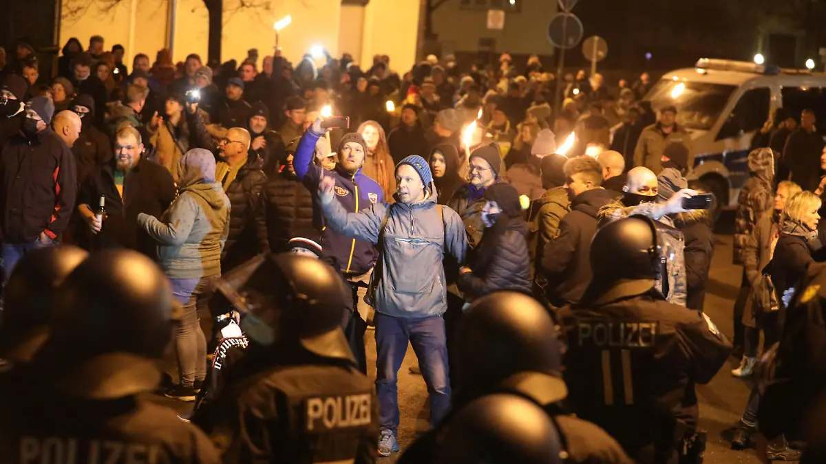 11.12.2021, Thüringen, Greiz: Polizisten und Teilnehmer eines so genannten Spaziergangs gegen die Corona-Maßnahmen stehen sich am Abend gegenüber. An der nicht genehmigten Demonstration beteiligten sich mehrere hundert Menschen. Foto: Bodo Schackow/dpa +++ dpa-Bildfunk +++
