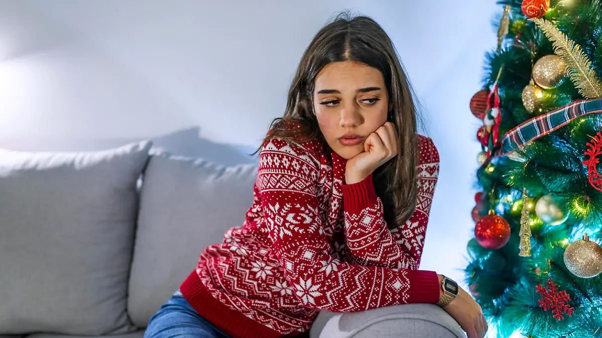 Woman feeling alone during christmas holiday. Portrait of frustrated young woman near christmas tree. Sad woman near the new year tree. Stressed young woman in front of christmas tree