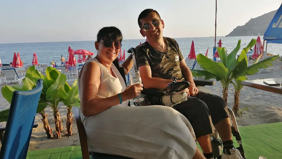Mann im Rollstuhl und Frau am Strand mit Getränken in der Hand.