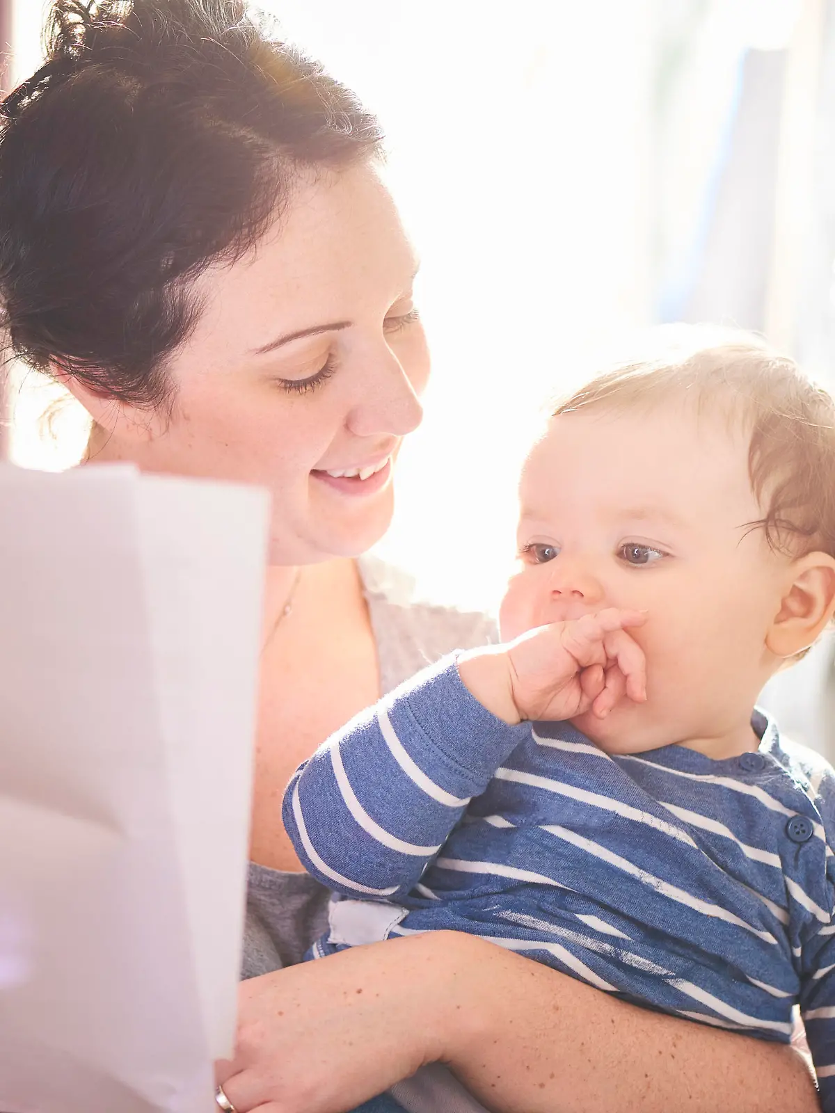 A young mother reads through a legal pack from her insurance company or solicitor. She is making provisions for the future of her child. The child is sat happily on her knee and the family dog is on the sofa next to them.