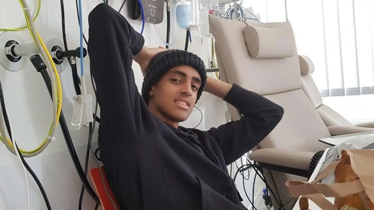 Colin sitzt auf einem Krankenhausbett und lächelt in die Kamera.