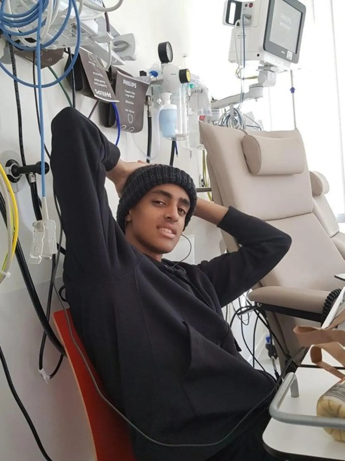 Colin sitzt auf einem Krankenhausbett und lächelt in die Kamera.